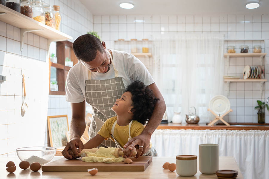 Personal Insurance - Father and Son Wearing Aprons Roll Out Cookie Dough in Their Country-Style Kitchen, With Eggshells and Baking Supplies Spread Out on a Wooden Counter